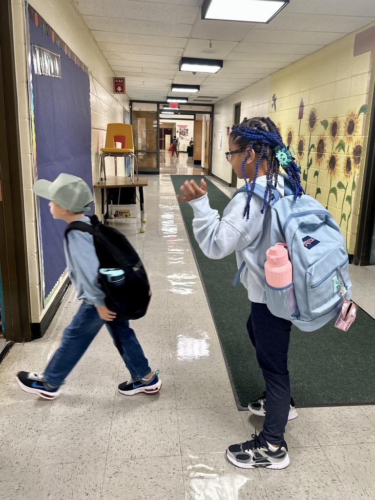 Two students with backpacks walk down a school hallway.