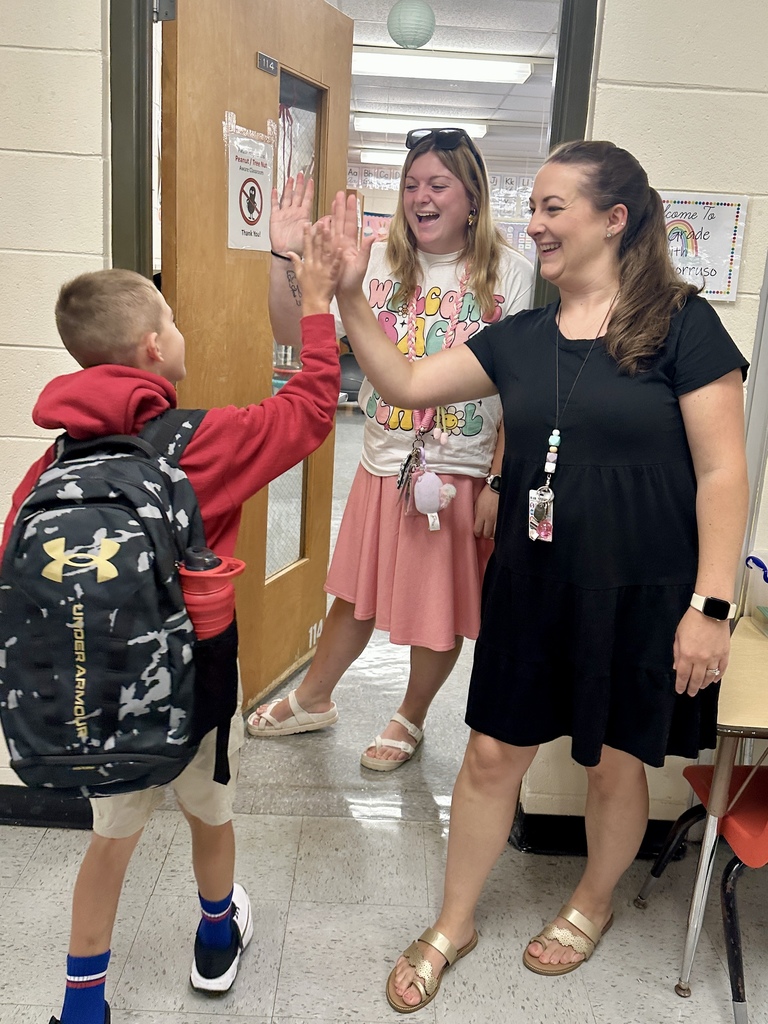 Teacher gives a high five to a student entering the classroom as another staff member looks on.