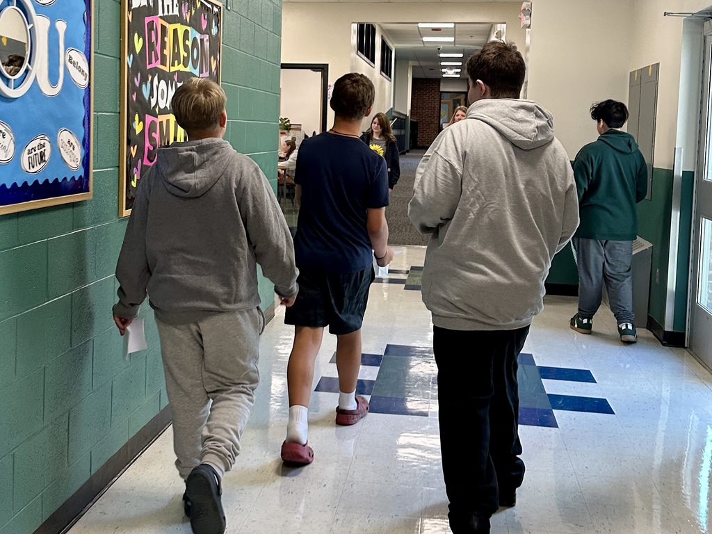Three boys walk down a school hallway together, carrying schedules and chatting.