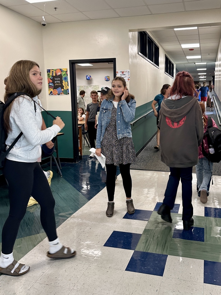 Students walk through a school hallway between classes, chatting and smiling.