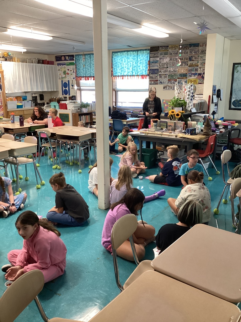 Students seated in groups on the floor of a decorated classroom, participating in an activity.