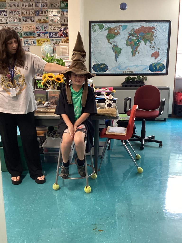 Teacher placing Sorting Hat on a student sitting on a stool in the classroom.