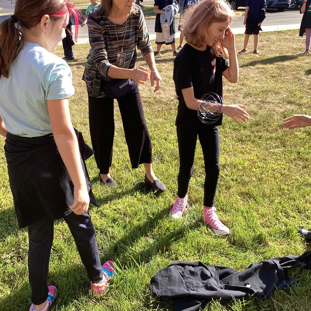 Teacher helping two students with a colorful magic ring activity outside on the grass.