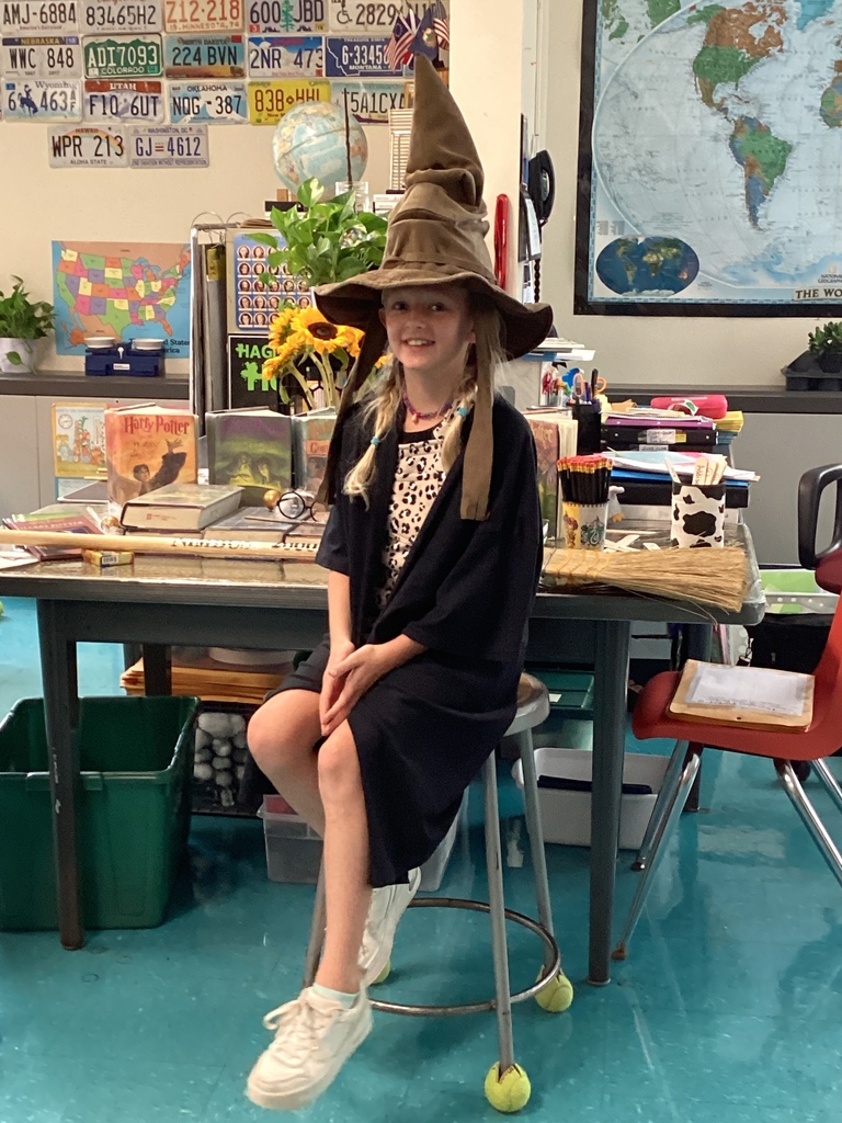 Student in a robe wearing the Sorting Hat while sitting on a stool inside a classroom.