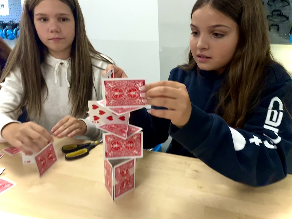 Two girls concentrate while stacking playing cards into a tower.