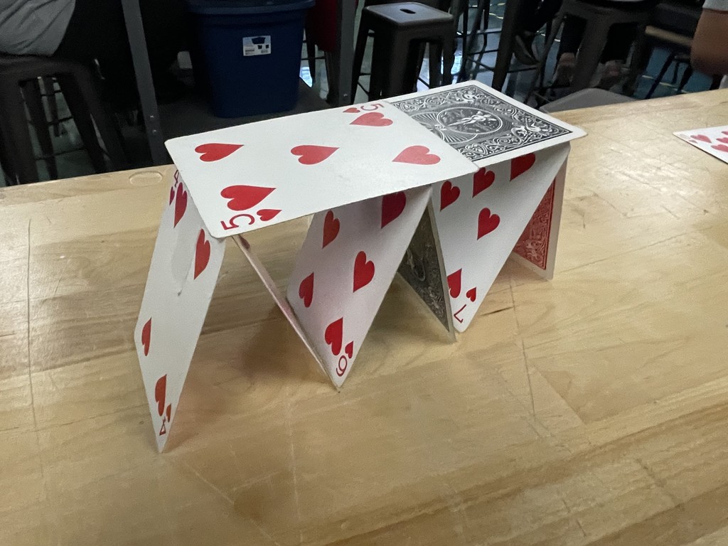 A small house of cards built from red and black playing cards on a wooden table.