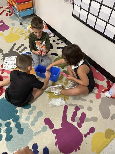 Kindergarten students practice switching between learning stations with bead activities.