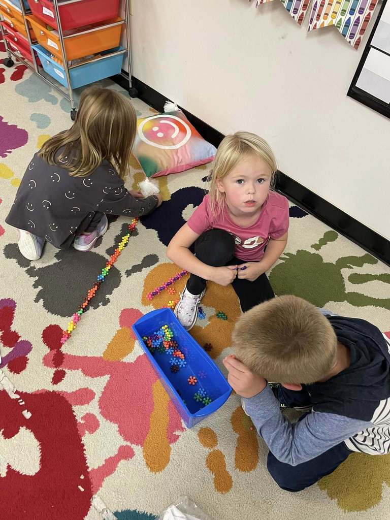 Kindergarten students practice switching between learning stations with bead activities.