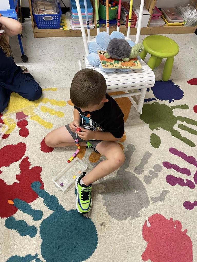 Kindergarten students practice switching between learning stations with bead activities.