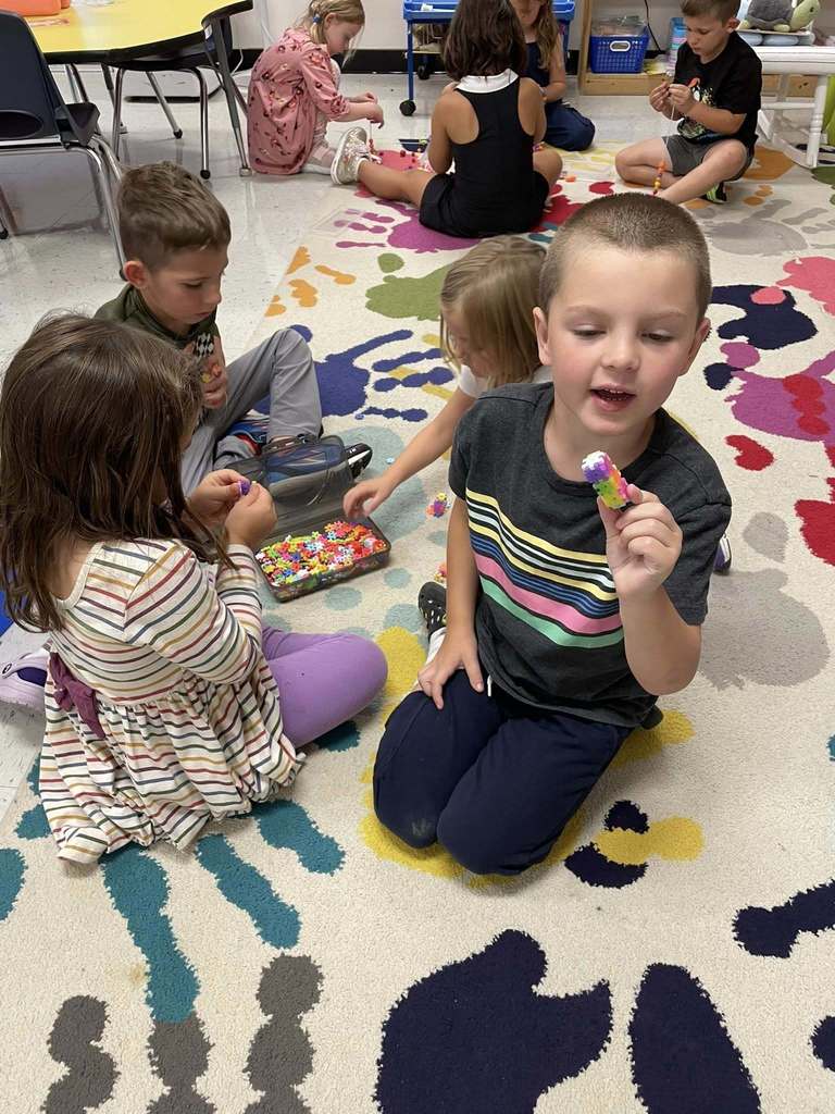 Kindergarten students practice switching between learning stations with bead activities.