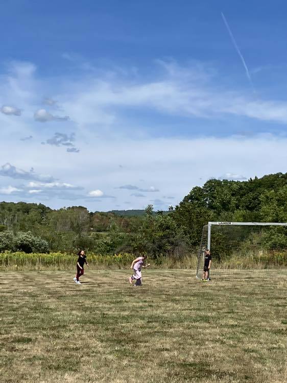 4th grade students play soccer on the school field under a sunny sky.