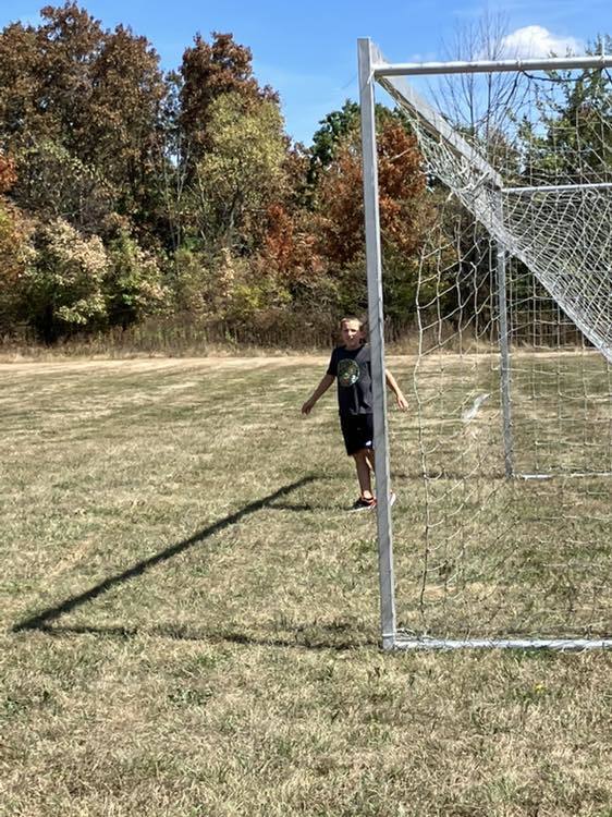4th grade students play soccer on the school field under a sunny sky.