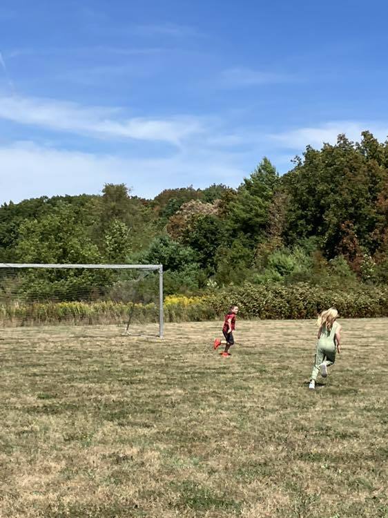 4th grade students play soccer on the school field under a sunny sky.