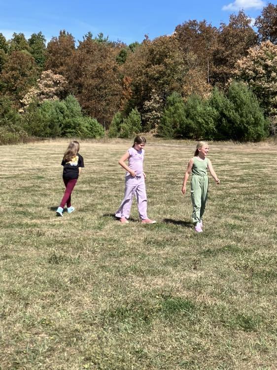 4th grade students play soccer on the school field under a sunny sky.
