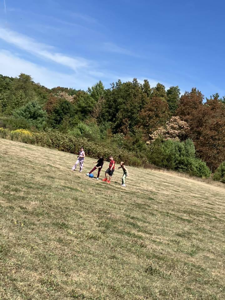 4th grade students play soccer on the school field under a sunny sky.