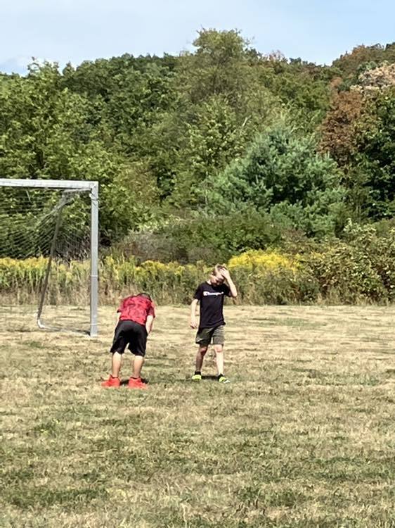 4th grade students play soccer on the school field under a sunny sky.