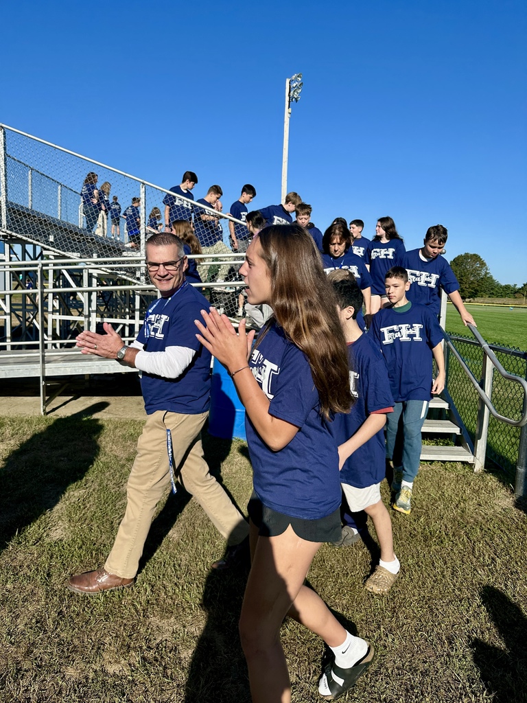 A teacher and students clap and smile while leaving the bleachers after the group photo.
