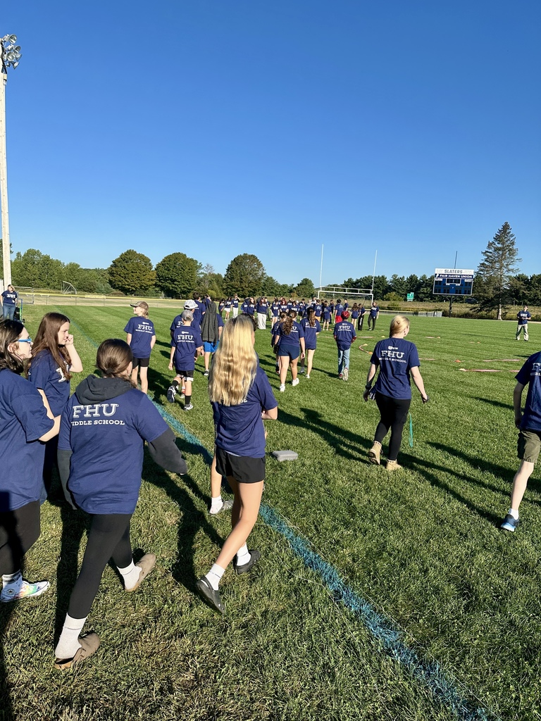 Students in FH shirts walk across the football field, heading toward a gathering area.