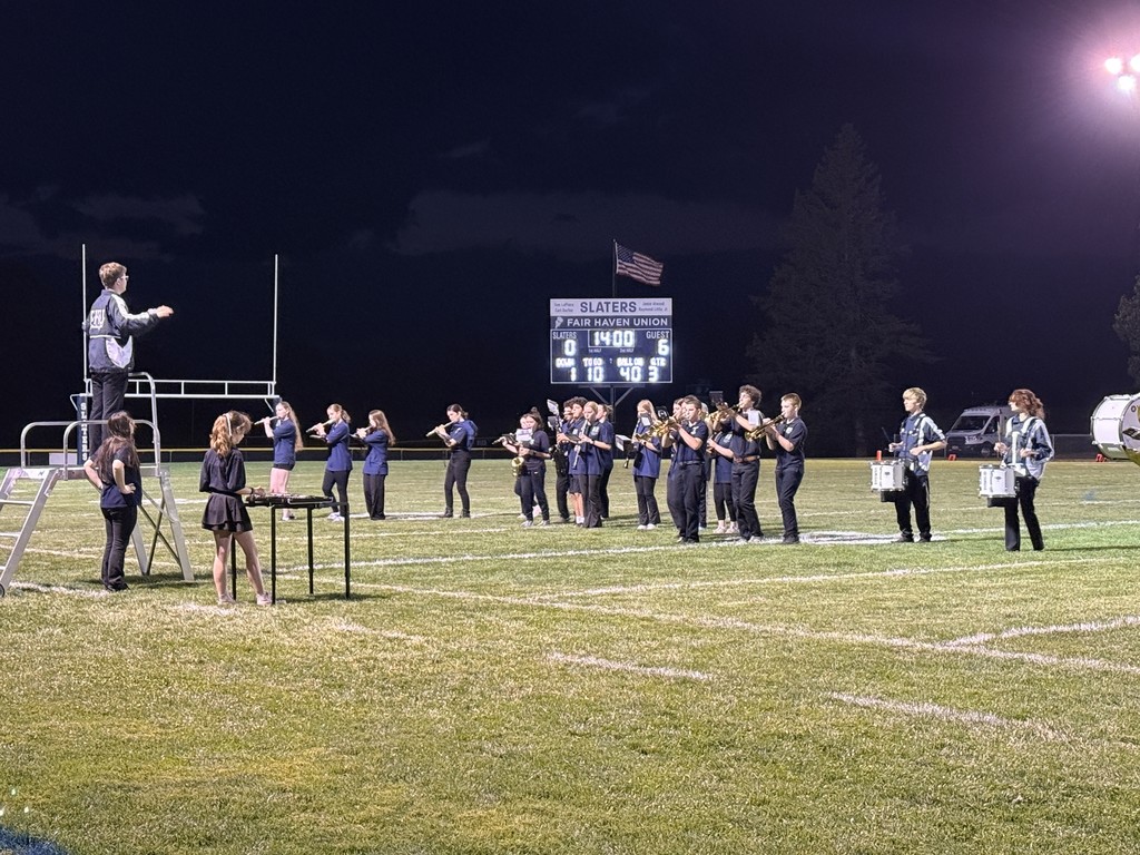 Fair Haven Union marching band performs on the football field at night under stadium lights, with a conductor leading from a podium.