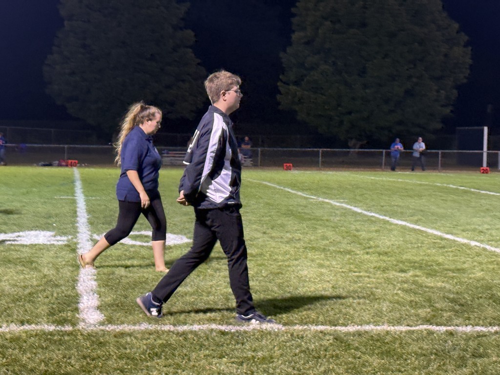 Student conductor walks across the football field with another student after the band’s performance.