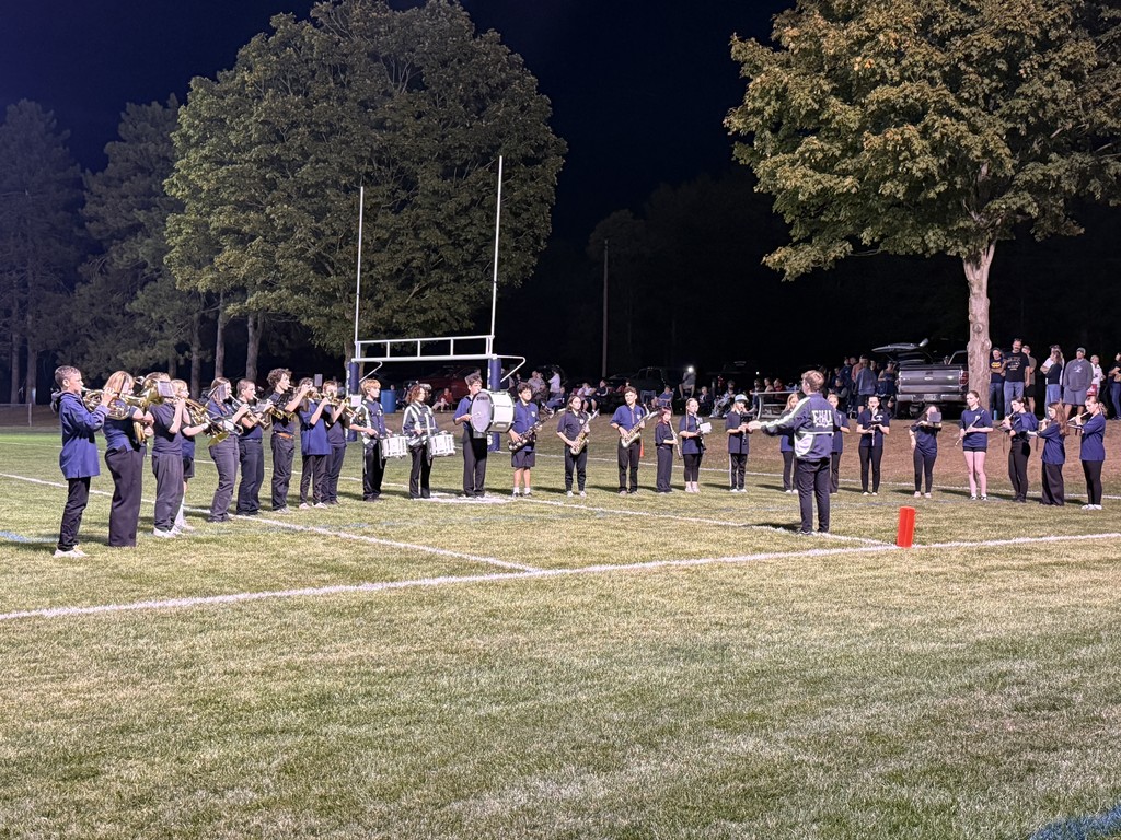 Marching band stands in formation across the football field performing for the crowd at night.