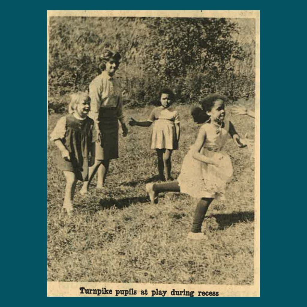 Black and white photo of Turnpike School pupils playing outside during recess, with children running and smiling in a grassy field.
