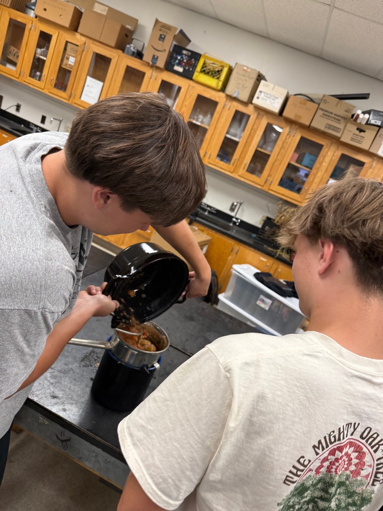 Two students pour cooked apples into a strainer over a pot.