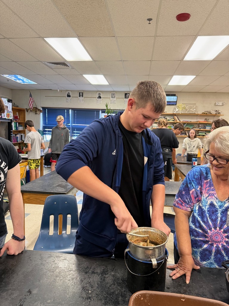 A student stirs applesauce in a pot while a teacher watches.