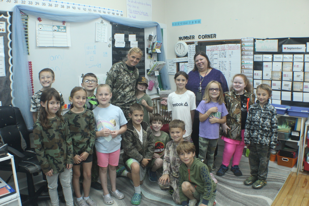 A group of children and two adults stand together in a classroom, smiling for a photo.