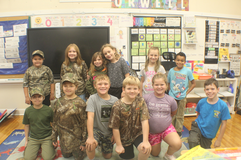 A group of ten students, some kneeling and some standing, smile for a photo in a classroom.