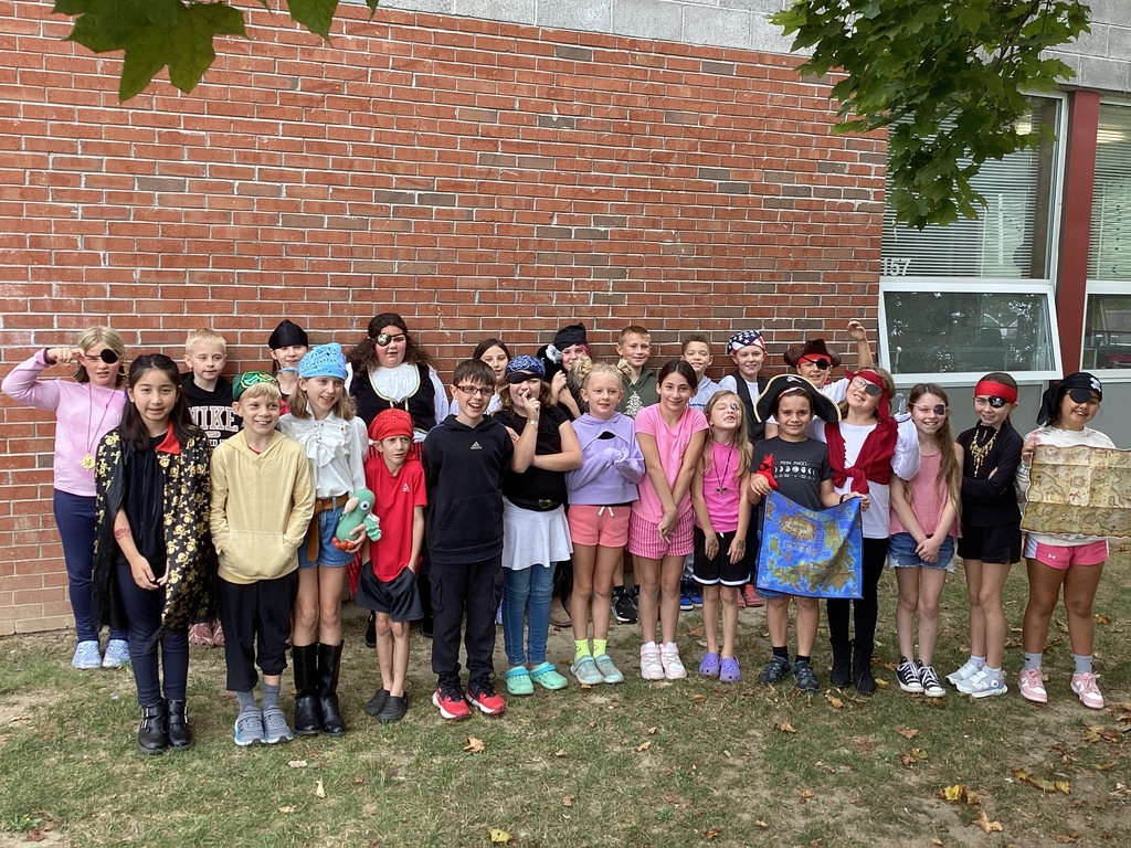 A large group of elementary students dressed as pirates stand together outside against a brick wall, smiling and posing.