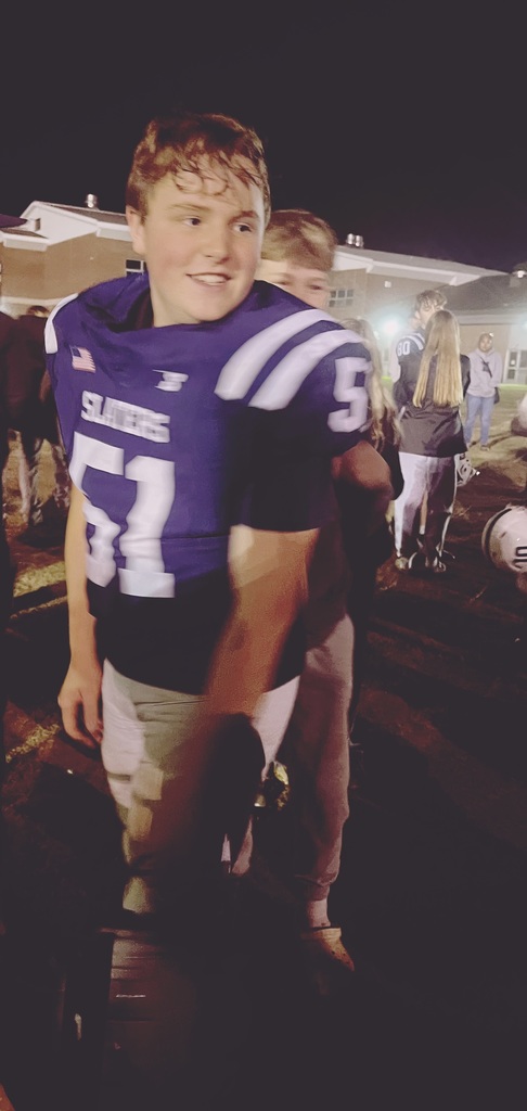 A smiling football player in a navy jersey with number 51 is surrounded by teammates and friends after a night game.