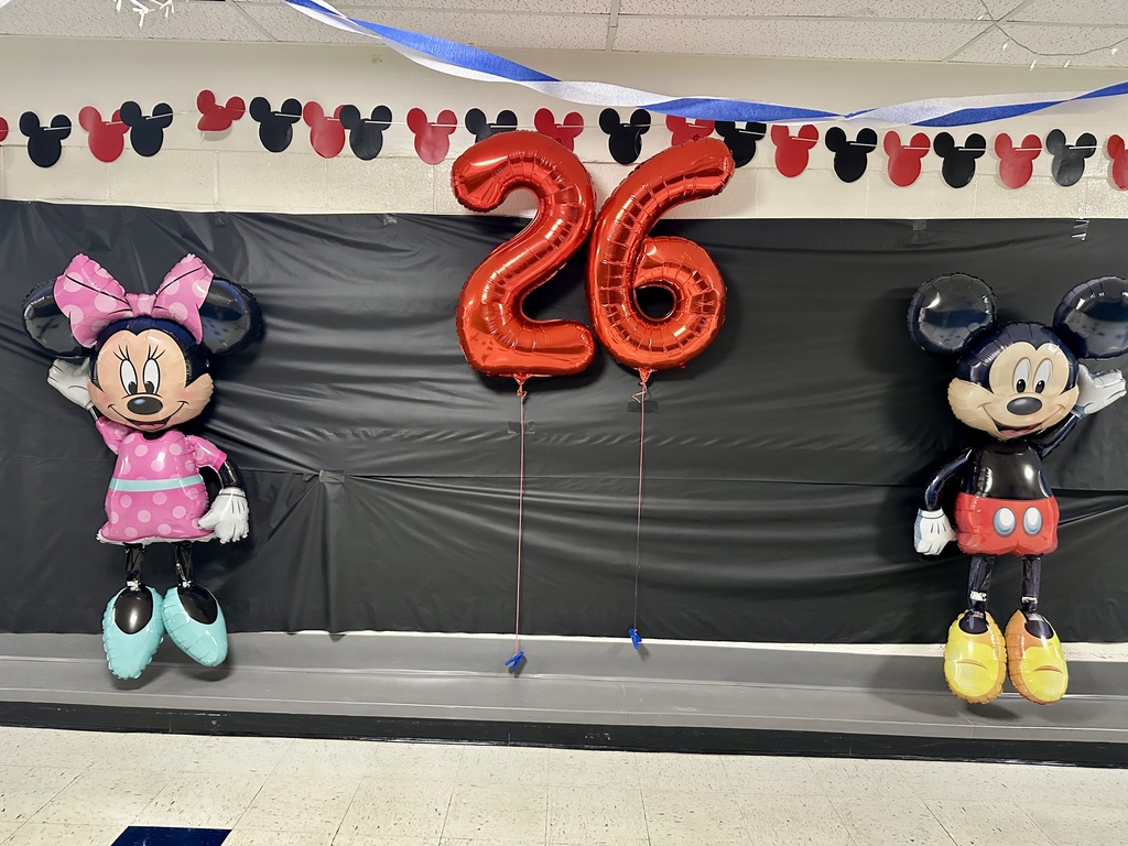 Large balloons of Minnie Mouse and Mickey Mouse with red “26” number balloons in between, set against a black backdrop with Mickey head cutouts.