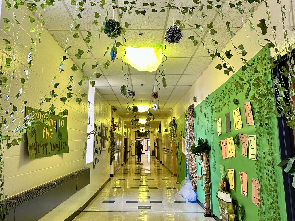 A school hallway decorated as a jungle with hanging vines, green streamers, and paper leaves. A wall display reads “Born to Be Wild” with jungle-themed art.