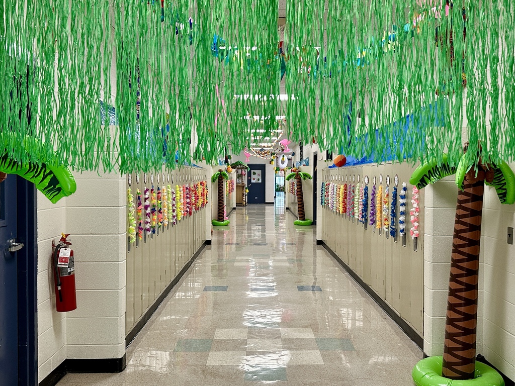 Hallway lined with lockers decorated with leis, inflatable palm trees, and green streamers hanging from the ceiling like jungle vines.