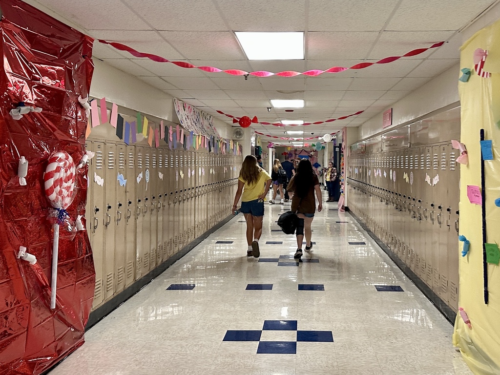 A school hallway with lockers decorated in a candy theme, including red and yellow walls covered in candy cutouts and hanging streamers.