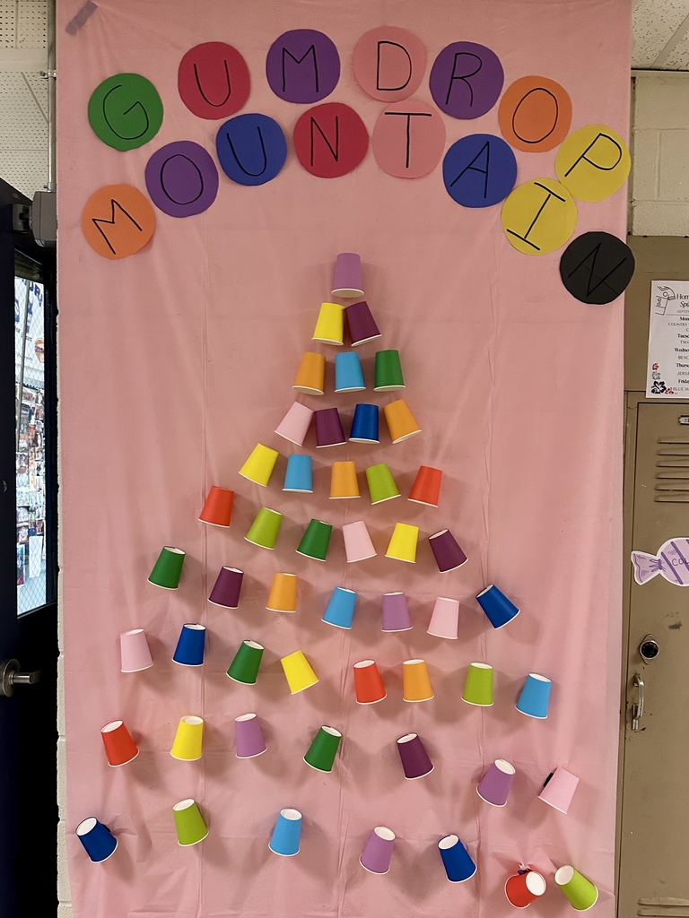 A wall decorated with a pink background, multicolored paper cups arranged like a tree, and the words “Gumdrop Mountain.