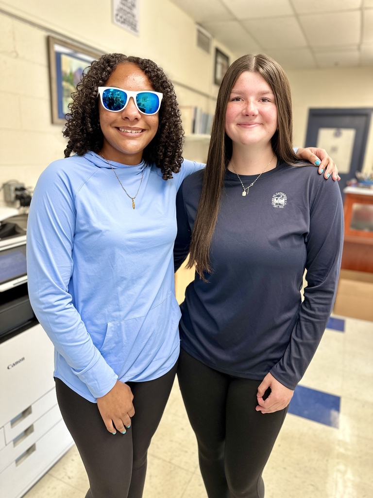 Two students smiling, one in sunglasses and a light blue top, the other in a navy long-sleeve shirt.