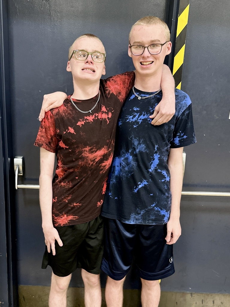 Two students with glasses standing arm in arm, wearing red and blue tie-dye shirts.