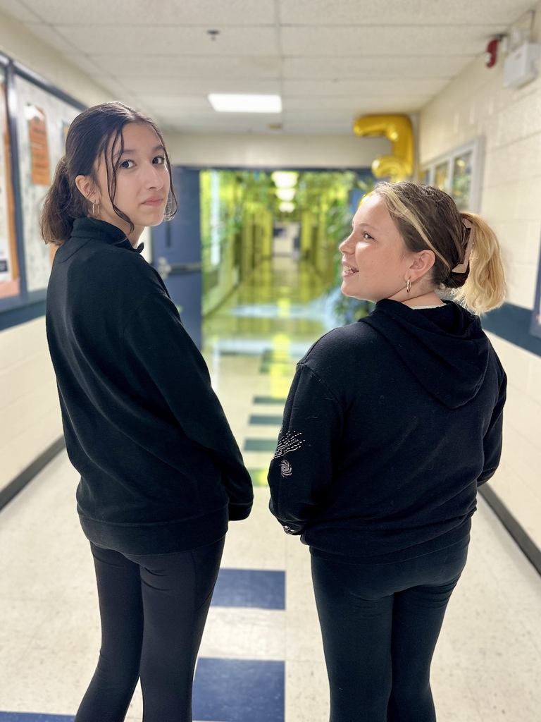Two students in black hoodies and leggings standing in a hallway decorated with green streamers.