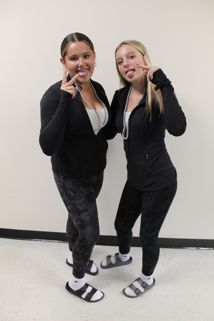 Two students in black outfits with silver necklaces, smiling and flashing peace signs.