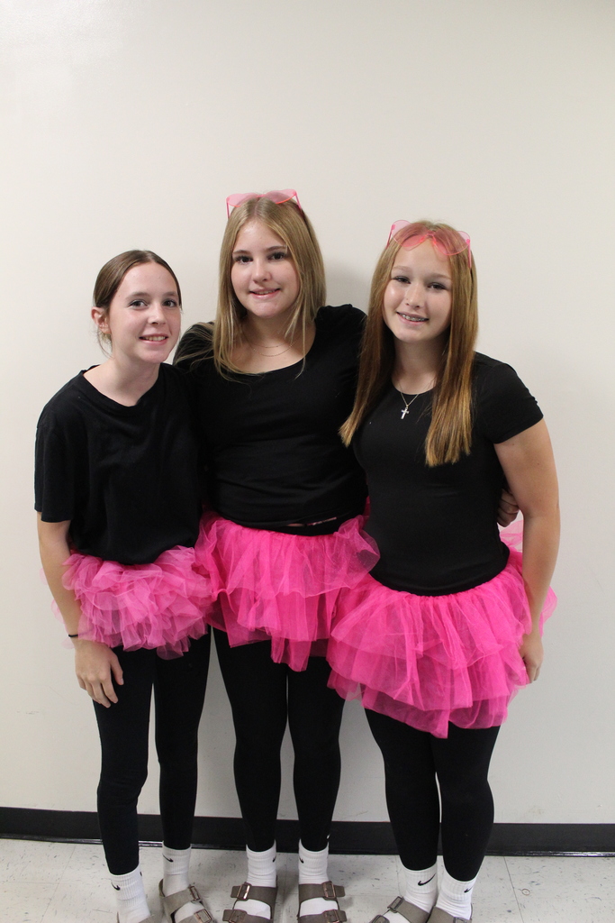Three students dressed in black shirts, leggings, and pink tutus, smiling together.