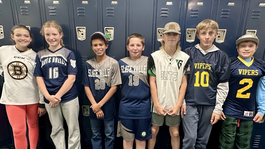 Seven middle school students line up in front of lockers wearing a mix of Slate Valley, Elite, and Vipers sports jerseys, smiling for the photo.