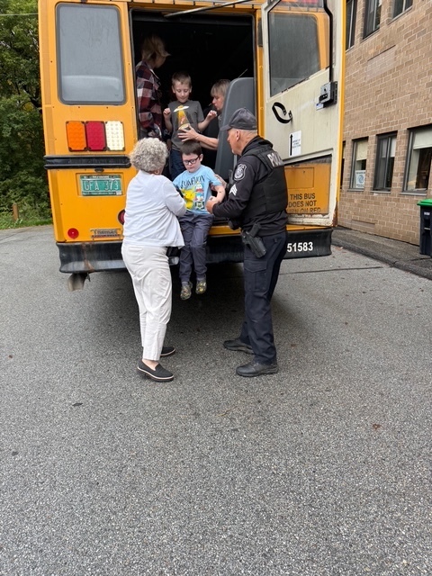 A police officer and an adult assist a small child stepping out of a school bus during a drill.