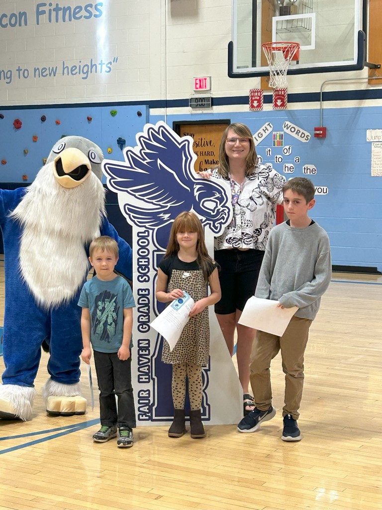 Three students holding certificates stand with the librarian, a falcon mascot, and a large SOAR sign in a school gymnasium.