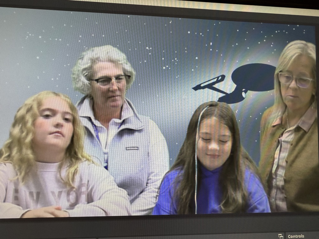A young boy and girl and two adult women are shown on a video screen. The background is a digital starfield with a silhouette of the Starship Enterprise from Star Trek.