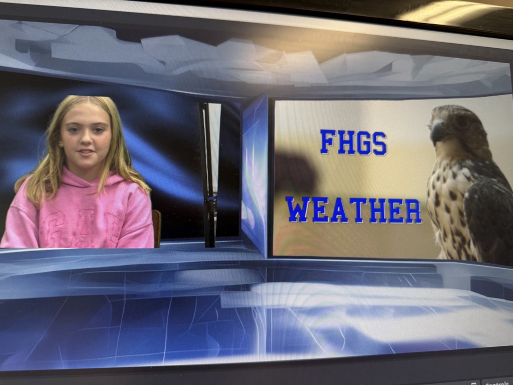 A girl wearing a pink sweatshirt sits on a chair. She is in front of a blue screen with a digital overlay that says "FHGS WEATHER" next to an image of a falcon