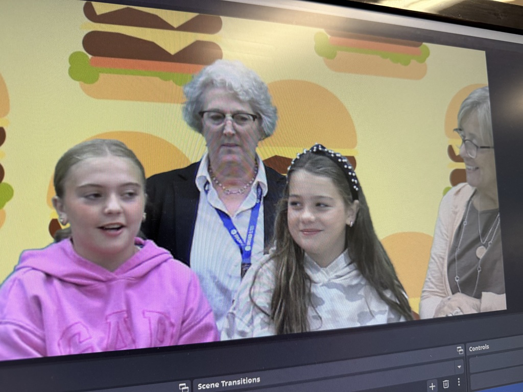 A group of people, including two young girls and two adult women, are shown on a video screen. The background is a repeating pattern of cartoon hamburgers.