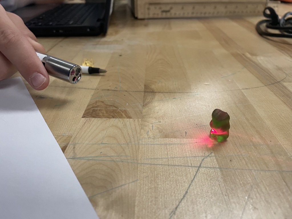 Close-up of a gummy bear on a table illuminated by a red laser light.