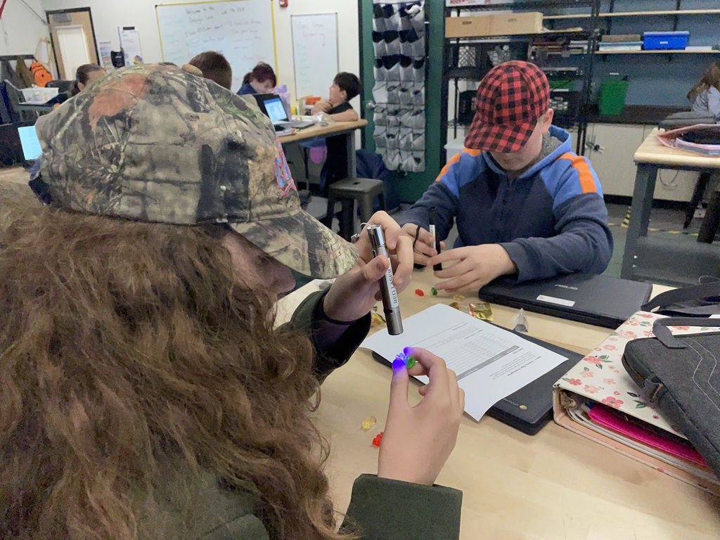 Students in hats shine colored laser lights on gummy bears during a classroom experiment.